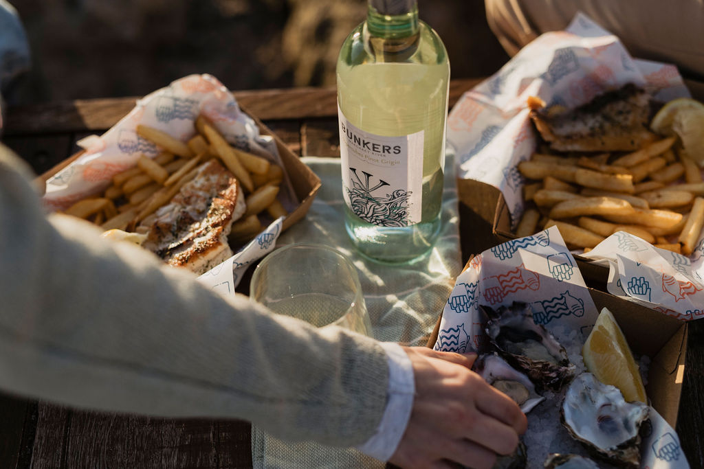 A person enjoying a bottle of Bunkers wine with oysters and fish and chips 